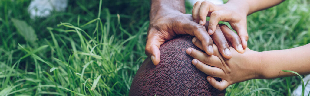 partial view of african american father and son touching rugby ball, panoramic shot